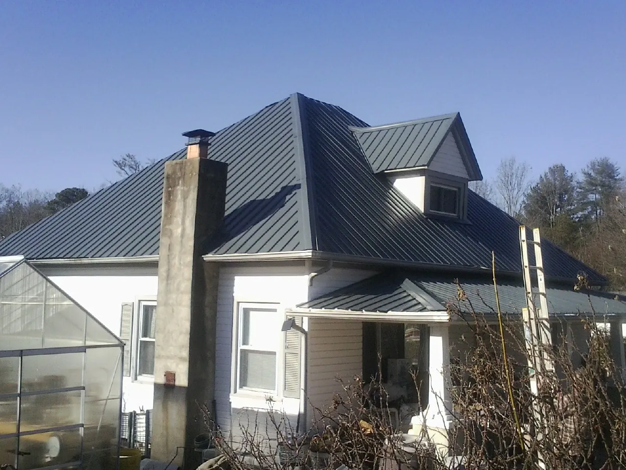 Dark blue standing seam metal roof on a white farmhouse with dormer — Slate & Tile Roof Repair by Roofing Brothers in Crystal Bay