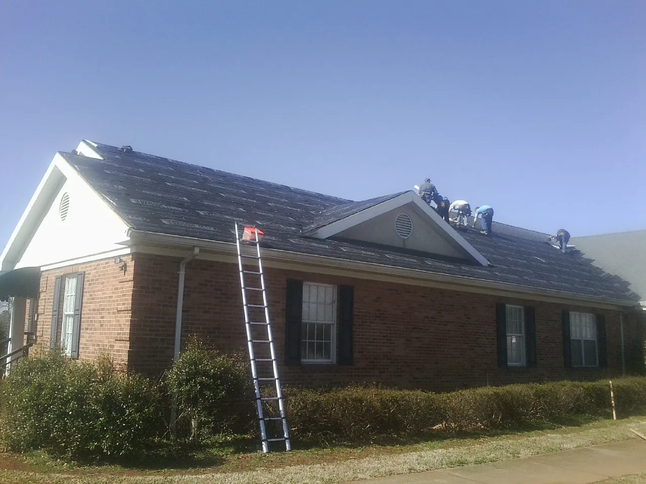 Crew tearing shingles off a brick ranch roof with a ladder set — Emergency Roof Repair work by our crew in Crystal Bay