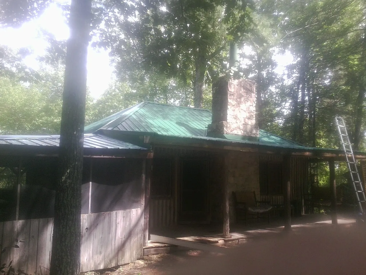 Green metal roof and stone chimney above a log cabin porch in Crystal Bay